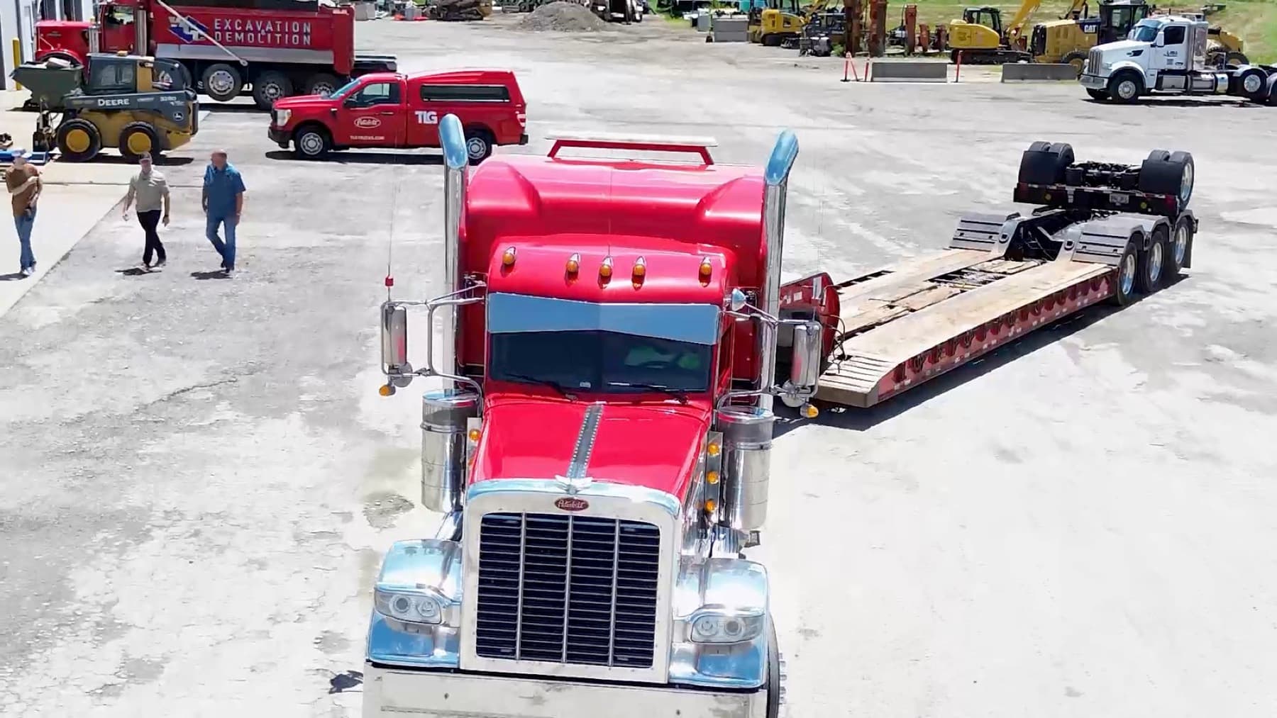 Red Peterbilt hooked to a lowboy trailer in a busy yard